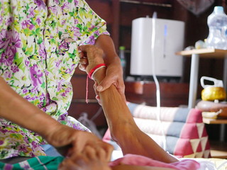 Hands of a woman holding / securing an older person's arm, while giving the elderly a bed bath with...