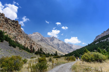 Fototapeta na wymiar Turkey, Chamard - August 3, 2019: Tourists walk along the road through the mountain landscape in the Turkish national Park aladag in summer day, view from the back