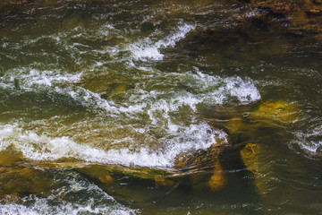 Small foamy waves among the clear water of a mountain river_
