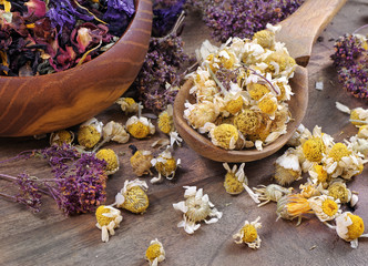 dried chamomile flowers in a wooden spoon, blended tea in a bowl and thyme on a wooden table....