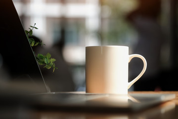 Cropped shot view Digital laptop and cup of coffee on old wooden desk. Simple workspace or coffee break in morning/ selective focus