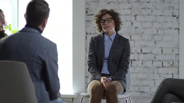 PAN of nervous young woman in glasses discussing problems with male and female patients during interpersonal psychotherapy session