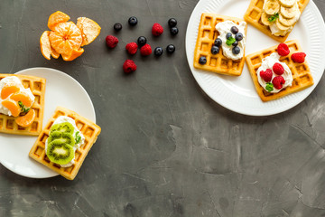 Fototapeta na wymiar Beautiful yummy snacks. Waffles with cream and friuits on grey background top-down frame copy space
