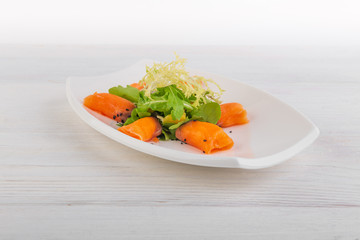 salmon rolls with arugula and salad with sesame on a white wooden background