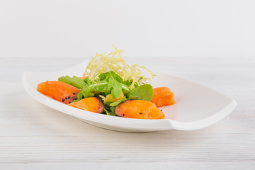 salmon rolls with arugula and salad with sesame on a white wooden background