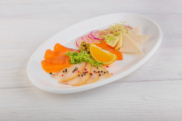 slicing of salmon, white fish with salad, onions and olives on a white wooden background