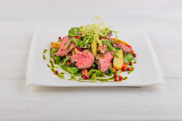 salad with potatoes and roast beef with green salad on a white wooden background