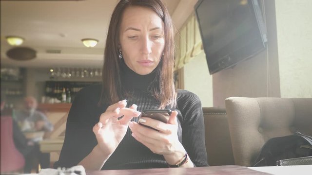 Young wonam use mobile phone while sitting in comfortable coffee shop during work break, charming happy female reading fashion news on cell telephone during breakfast in restaurant.