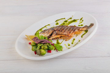 whole baked fish with brussels sprouts, pesto sauce on a white wooden background
