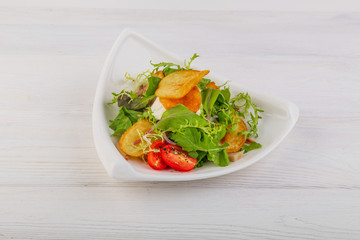 potato chip salad, greens and cherry tomatoes on a white wooden background