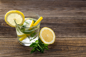 Water with lemon and mint in a glass on wooden background. Summer fresh lemonade drink