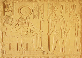 Fototapeta na wymiar Yellow plaster bas-relief with the gods of ancient Egypt, the God Amon-RA, Horus and the two goddesses
