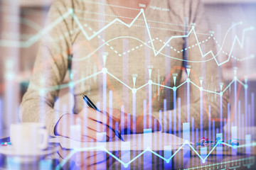 Hand taking notes in notepad. Forex chart holograms in front. Concept of research. Double exposure