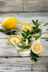 Two glasses of lemonade with lemon, mint and ice cubes on wooden background. Summer drink