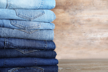Stack of different jeans on wooden table. Space for text