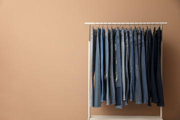 Rack with stylish jeans near beige wall. Space for text