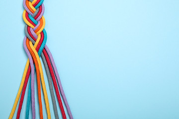 Top view of braided colorful ropes on light blue background, space for text. Unity concept - obrazy, fototapety, plakaty