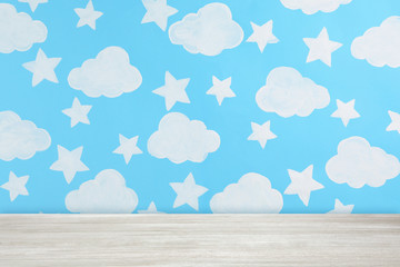 Fototapeta na wymiar Wooden table near wall with painted clouds and stars. Idea for baby room interior design