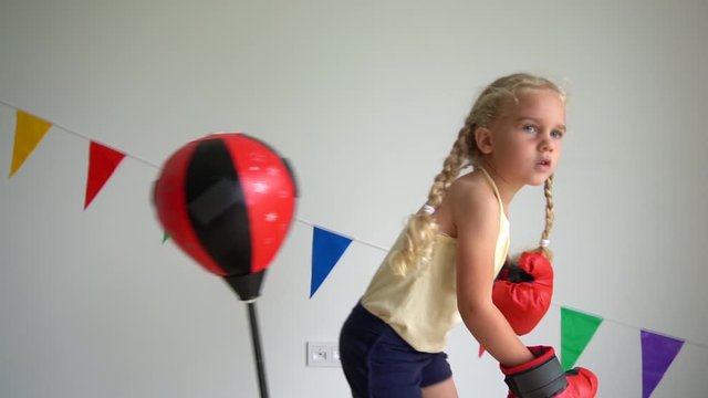 little child girl box with gloves on punching bag. slow motion