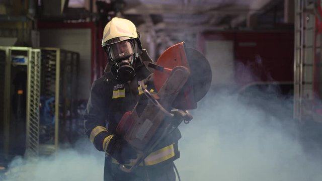 firefighter portrait wearing full equipment, oxygen mask, and power hydraulic cutting tool, smoke and fire trucks in the background. Name tag translation is fireman and model's last name.