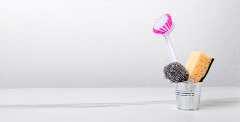 Tiny metal bucket and sponge, cleaning brush, scrubber in it. Cleaning tools on the white table...
