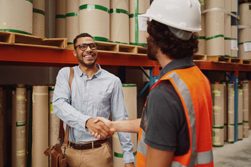 Happy banker in formal clothing shaking hands with warehouse manager after granting him his loan