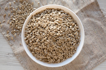 Top view, Raw Sunflower Seed Kernels in a white bowl on a white wooden surface. Flat lay, overhead, from above.