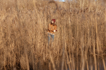 Young woman near lake in high dry field grass smiles and embraces herself. Girl in nature.