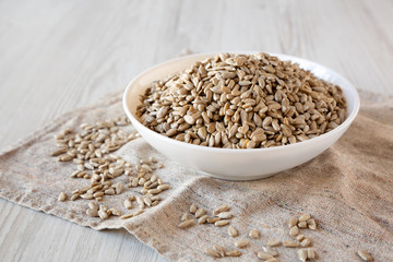 Raw Sunflower Seed Kernels in a white bowl on a white wooden background, side view. Close-up.