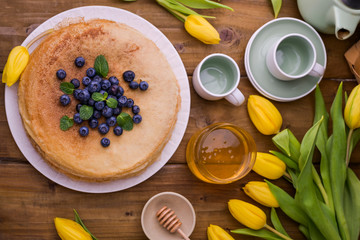 Large traditional Russian pancakes with berries and honey on a wooden table. Baking for the spring holiday Shrovetide and a bouquet of yellow tulips. Copy space