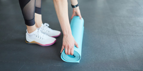 Woman rolls a yoga mat together after workout