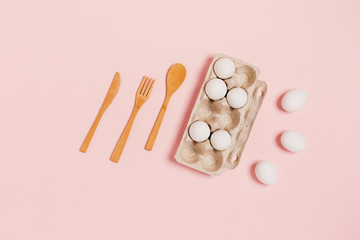 Photo on kitchen theme. Chicken eggs in recycled paper packaging and bamboo cutlery on pink background. Flat lay, top view, copy space.