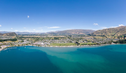 Obraz na płótnie Canvas Beautiful panoramic high angle aerial drone view of the town of Wanaka, a popular ski and summer resort town located at Lake Wanaka in the Otago region of the South Island of New Zealand.