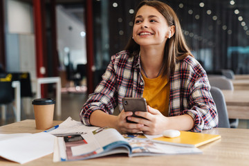 Image of happy nice girl using wireless earphone and cellphone