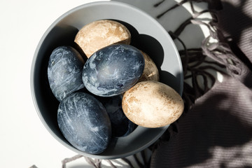 Easter background with Easter eggs and feathers in a ceramic gray bowl. Background with easter eggs. Naturally dyed eggs prepared for Easter on gray texture tablecloth background. Happy Easter