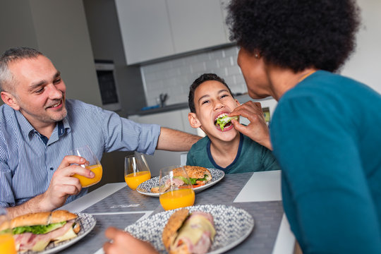 Smiling Mixed Race Family With They Son Sitting At The Kitchen Table Having Breakfast At Home.