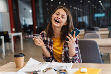 Image of delighted cute girl holding credit card and cellphone