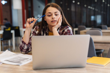 Image of serious girl doing homework with laptop and exercise books