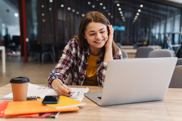 Fototapeta premium Image of smiling girl doing homework with laptop and exercise books