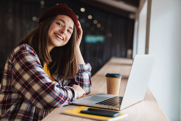 Image of joyful caucasian girl smiling and using laptop while sitting