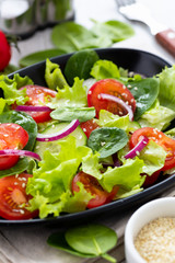 Healthy vegetable salad from fresh vegetables of tomato, spinach, cucumber, lettuce and sesame on a plate. Useful nutrition.