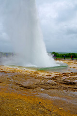 People waiting for Big Geysir erruption or Strokkur to errupt in geothermal field with hot springs...