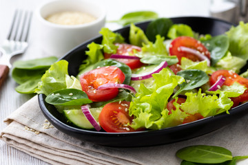 Healthy vegetable salad from fresh vegetables of tomato, spinach, cucumber, lettuce and sesame on a plate. Useful nutrition.