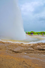 People waiting for Big Geysir erruption or Strokkur to errupt in geothermal field with hot springs...