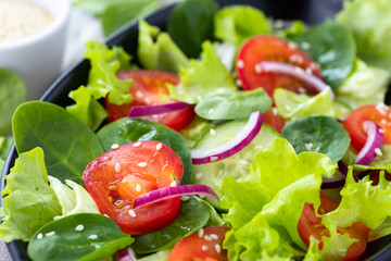 Healthy vegetable salad from fresh vegetables of tomato, spinach, cucumber, lettuce and sesame on a plate. Useful nutrition.
