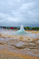 People waiting for Big Geysir erruption or Strokkur to errupt in geothermal field with hot springs...