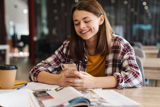 Image of joyful caucasian girl using cellphone while doing homework