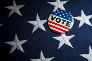 Vote political election pin sitting on thick textured American flag background