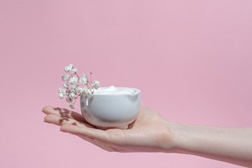 a jar of cream in a woman’s hand, white texture, flowers, natural composition, SPA care and massage
