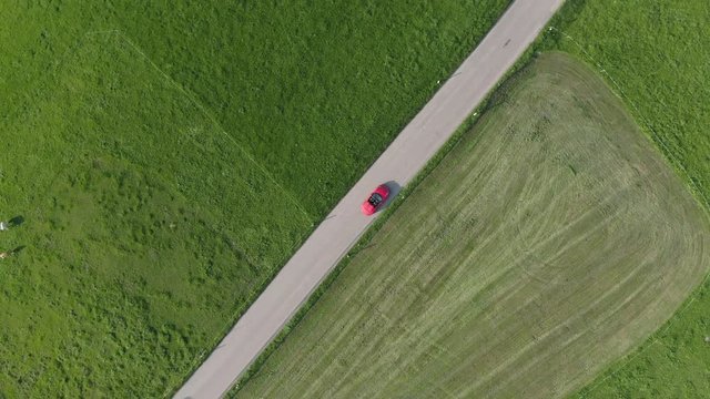Top down aerial shot of red sportscar cabriolet driving on beautiful road through green fields
